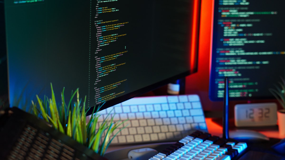 Multiple monitors displaying colorful coding text in a modern developer home office setup with ambient lighting